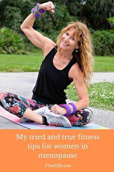 a woman sitting on top of a yoga mat with her arms in the air and holding up