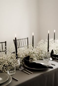 the table is set with black and white plates, silverware, and baby's breath flowers