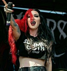 a woman with red hair and piercings on her chest holding a microphone in one hand