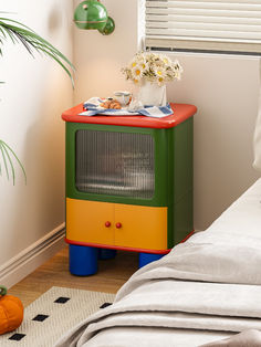 a bedroom with a bed and a colorful cabinet next to a plant on the floor