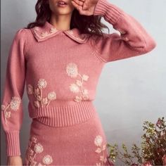 a woman in a pink sweater and skirt posing for the camera with her hand on her head