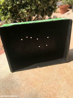 a black box with holes in it sitting on top of a cement surface next to a tree