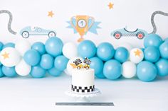 a birthday cake sitting on top of a table next to blue and white balloons in the shape of race cars