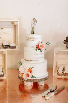 a wedding cake sitting on top of a wooden table next to cupcakes and utensils