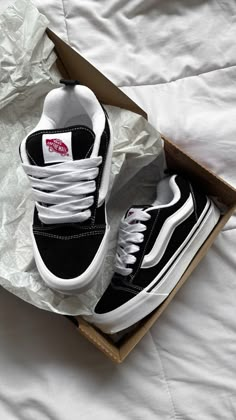 a pair of black and white shoes sitting in a box on a bed with sheets