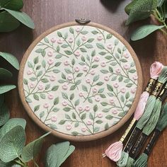 a close up of a embroidery on a wooden surface with flowers and leaves around it