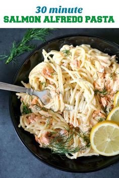 a black plate topped with pasta and shrimp next to lemon wedges on top of a table