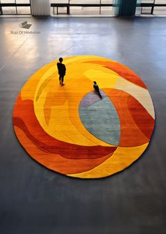 two people standing in front of a circular rug with an orange and yellow design on it