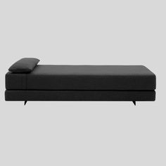 a black couch with two pillows on the top and one pillow on the bottom, in front of a gray background