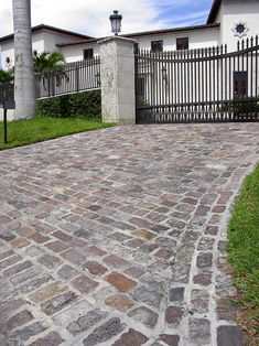 an image of a brick driveway in front of a house with a gate and palm trees