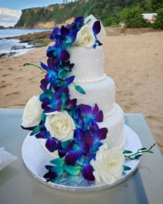 a white and blue wedding cake sitting on top of a table next to the ocean