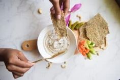 two hands holding spoons over a white bowl filled with peanut butter and veggies