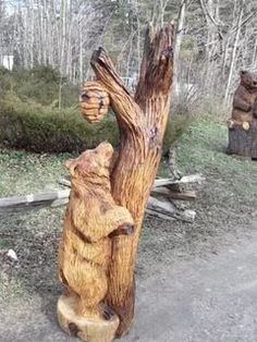 two carved wooden bears sitting next to each other on the side of a dirt road