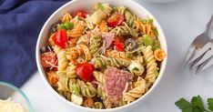 a white bowl filled with pasta salad next to a blue napkin and silverware on a table