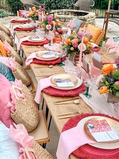 a long table set up with pink and gold place settings for an outdoor dinner party