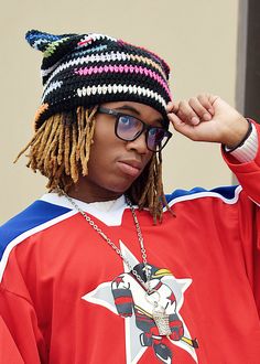 a young man with dreadlocks wearing a red hockey jersey and holding his hand on his head