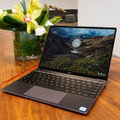 an open laptop computer sitting on top of a wooden table next to a vase with flowers