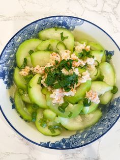 a blue and white bowl filled with cucumbers, herbs and other food items