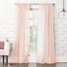 a white chair sitting in front of a window with pink curtains on the windowsill