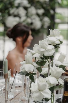 a woman sitting at a table with white flowers in vases and candles on it