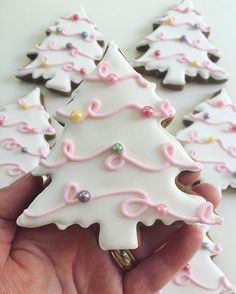 a hand holding some decorated cookies in the shape of christmas trees with pink and white icing