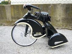 an old fashioned black and white motorcycle parked on the side of a road next to a cement wall