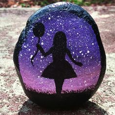 a painted rock with a silhouette of a girl holding two balloons in the night sky