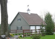 a large gray barn with a white steeple on top and a wooden fence around it