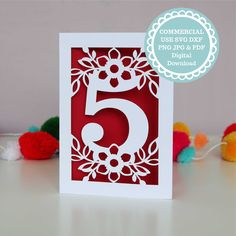 a red and white card with the number five on it, surrounded by pom poms