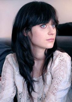 a woman with long black hair and blue eyes looking off into the distance while sitting on a couch