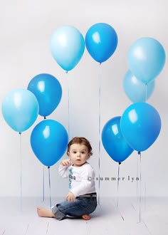 a baby sitting on the floor with blue balloons in front of her and an orange sign that says feliz cumpleanos