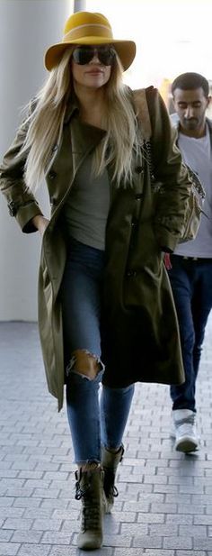 a woman in a hat and trench coat is walking down the street with another man behind her