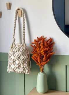 an orange flower in a vase next to a white purse on a wall with hooks