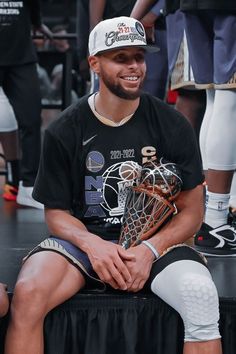 a young man sitting on top of a basketball court holding a trophy and smiling at the camera