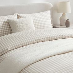 a bed with white and brown checkered comforter next to a lamp on a nightstand