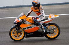 a man riding on the back of a motorcycle down a race track in an orange and black outfit