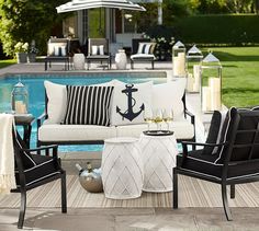 an outdoor seating area with chairs, table and umbrella next to a swimming pool in the background