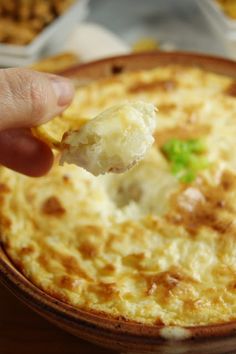 a hand holding a piece of food over a bowl filled with cheese and broccoli