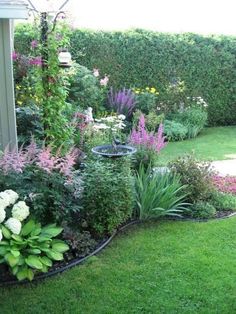 a garden filled with lots of different types of flowers and greenery next to a house