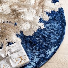 a white christmas tree with blue and gold ornaments on it next to a gift box