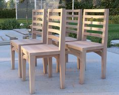 three wooden chairs sitting next to each other on a cement floor in front of a park