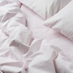 an unmade bed with white sheets and pillows