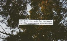 a sign hanging off the side of a tree in front of a blue sky that says slow down you're doing, you can't be everything