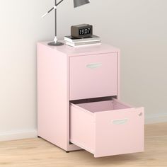 a pink filing cabinet with two drawers and a clock on top, next to a lamp