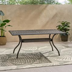 a patio table sitting on top of a rug next to potted plants and a wall