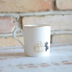 a white coffee cup with a black cat on the side and a brick wall behind it