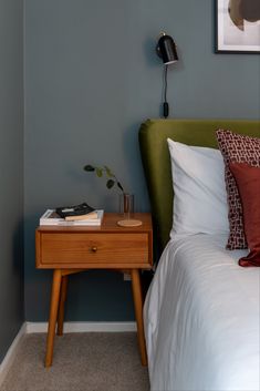 a bedroom with a green headboard and white sheets on the bed next to a nightstand