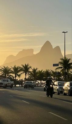 the motorcyclist is driving down the street in front of mountains and palm trees