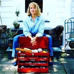 a woman sitting on top of a red tool box filled with tools next to a dog