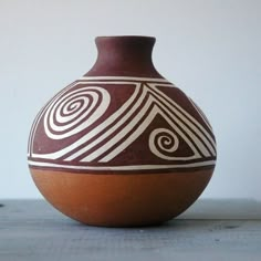 a brown and white vase sitting on top of a wooden table next to a wall